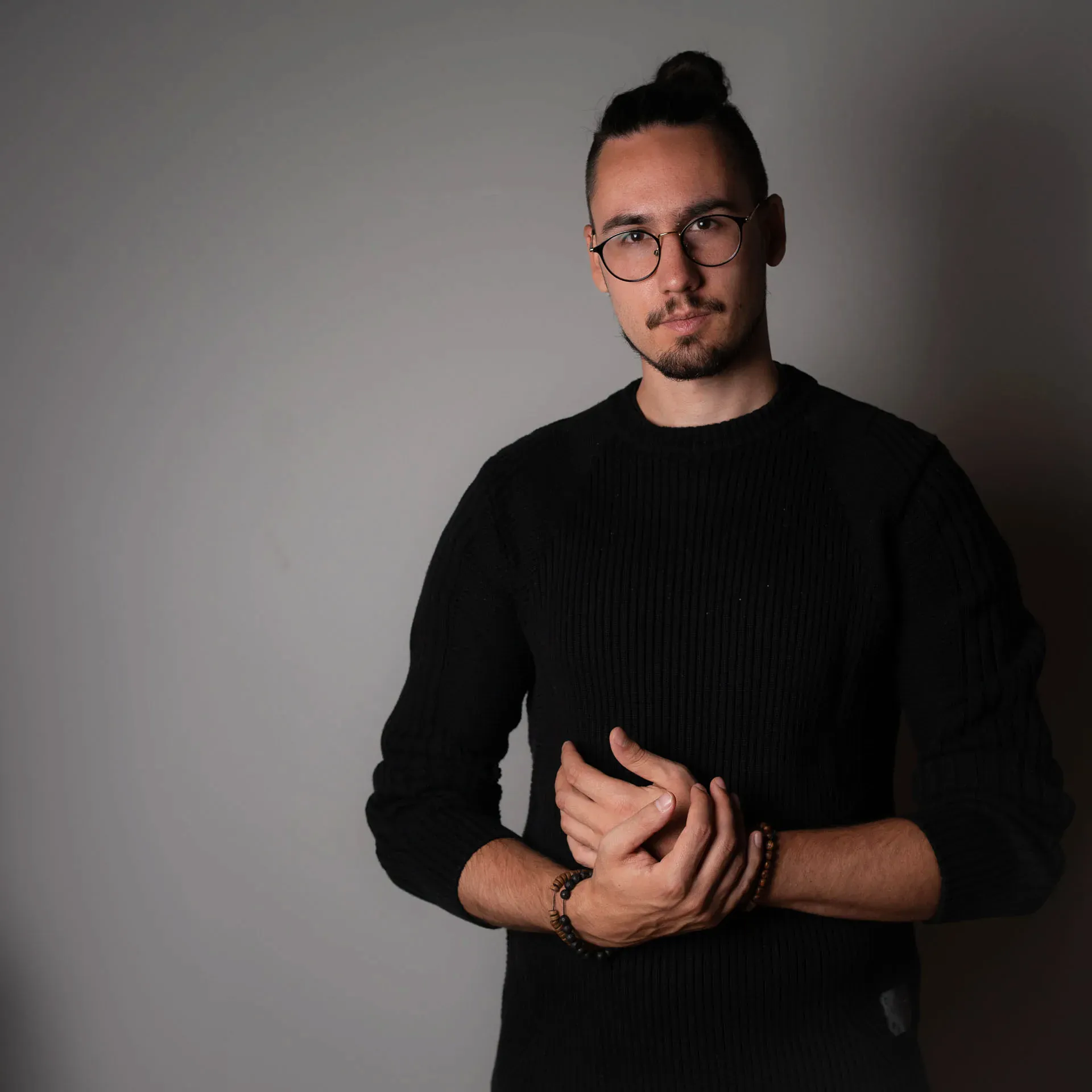 Toni Hofmann im schwarzen Strickpullover vor grauer Wand